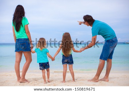 Back view of young family with two daughters at exotic beach on sunny day