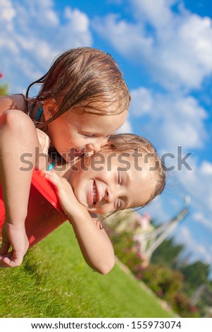 Two charming little happy sisters having fun in small pool on the courtyard outdoor