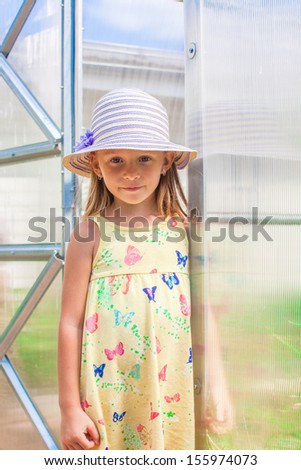 Little cute girl standing in a greenhouse at the garden of her house