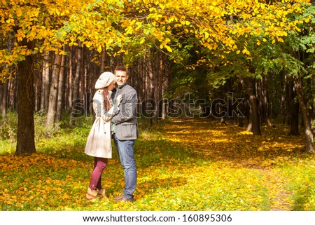 Young couple in love on the big autumn meadow under large maple tree at sunny fall day