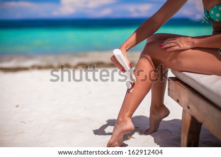 Young woman apply cream on her smooth tanned legs on tropical beac