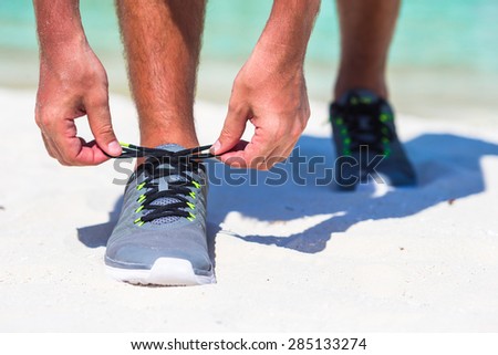 Running man tying running shoe laces on white beach