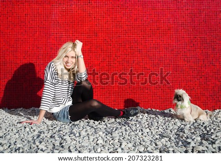 Pekingese dog in a green scarf sitting on a red background and the rocks near his mistress