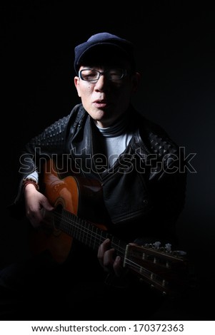 Portrait of a Japanese man with guitar/Japanese musician/A low key portrait of a middle aged Japanese man playing guitar with a cap and leather jacket posing dramatically