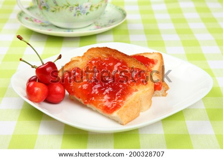 Jam toast with cherries/Jam toast/A photo of jam toast with fresh cherries on a checked cloth with teapot in background.
