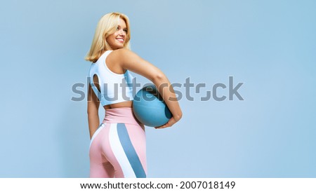 Portrait of a fitness happy fit woman standing holding a medicine ball. Copy Free space for text. Slim caucasian cross fit woman with fitness ball stand in gym, look. Plain light wall background