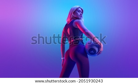 Confident fitness woman posing with a medicine ball. Attractive blonde sportswoman portrait holding with medicine fitness ball neon style creative light.