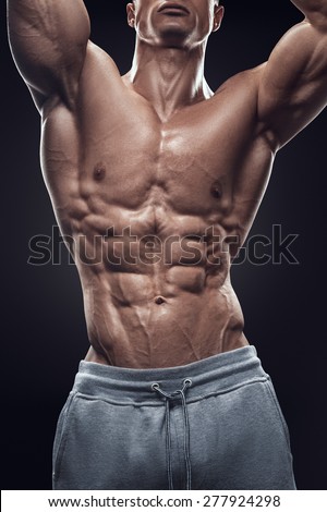 Strong athletic man fitness model torso showing six pack abs. Isolated on black background.