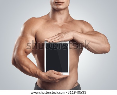 Close up photo of a handsome young fitness male model holding vertically digital tablet with blank screen, isolated on white background