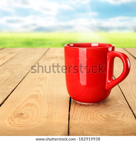 warm red mug of drink and summer landscape with grass and sky of blue
