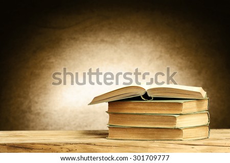 brown wall with shadow open book and three books on dirty wooden table