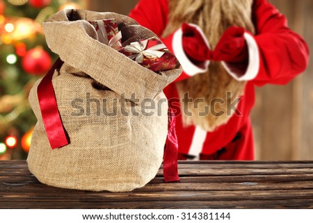 blurred background of xmas tree in home and red santa claus with sack of gifts and free space on top