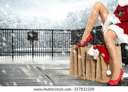 woman long legs in red heels and red santa claus hat on brown few bags on wooden terrace and space for your text