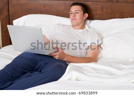 A handsome young man works on a laptop computer in bed