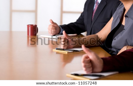 Business people in meeting with thumbs up gesture.  Shallow depth of field with middle hand in focus.