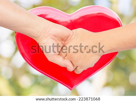 hand in hand with red heart and blur background