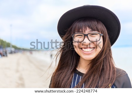asia teenage girl with eyeglasses and hat with blur beach background
