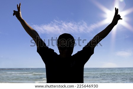 Silhouette of a man show his hand with victory sign at the beach