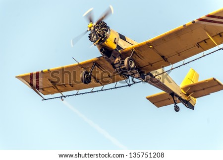 Closeup of a yellow agricultural aircraft in action while spraying mosquitoes. Low angle view over clear blue sky.
