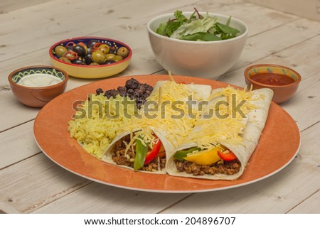 Burritos filled with ground beef and peppers with rice and beans on the side