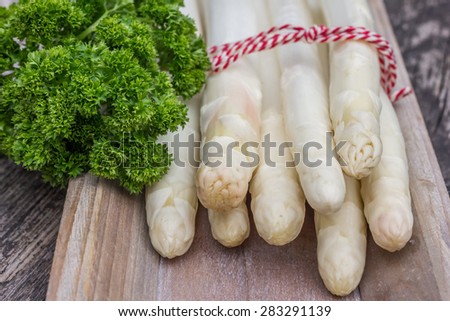 Bundle of white asparagus  with parsley on a wooden rustic plate