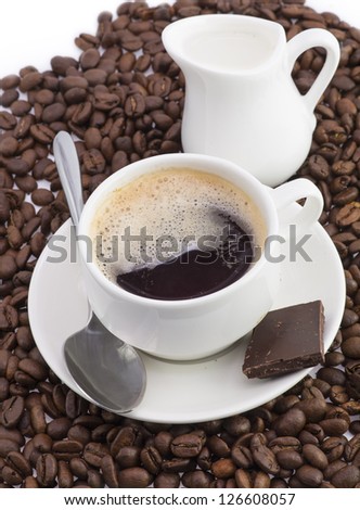 A cup of coffee flavored with chocolate and milk is on the background of coffee beans.