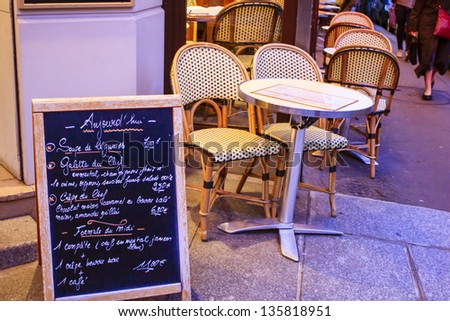 Evening scene in Paris - sidewalk cafe on the corner of the street with traditional circular tables and wicker chairs and menu exposed on the blackboard, Paris, France