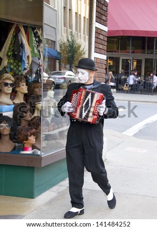 Asheville, North Carolina, USA - June 23, 2007: A mime street performer walks down the street playing an accordion in Downtown Asheville, North Carolina.