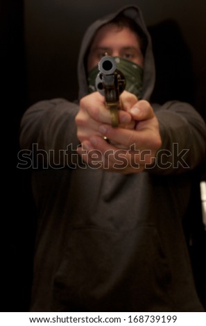 Masked man with a hood pointing a hand gun