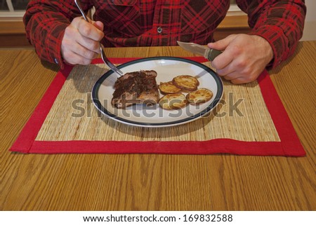 A man wearing a flannel shirt eating a plate of ribs.