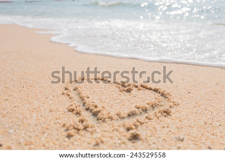 couple drawing a heart on wet golden beach sand