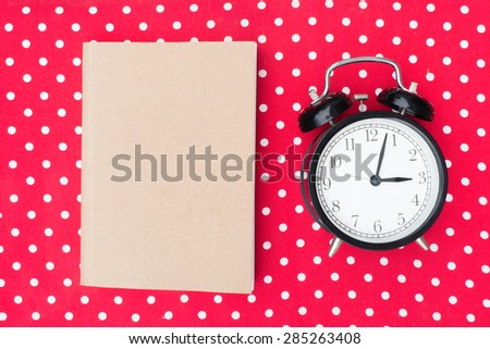Retro alarm clock and notebook on red polka dot background