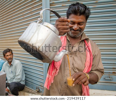 MYSORE, INDIA - FEBRUARY 8, 2013 - Men pours cup hot milk tea Indian style or chai for customers from his shop along street