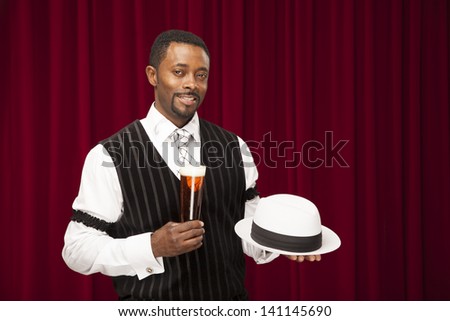 Well dressed African American in retro suite holding his hat and a glass of beer.