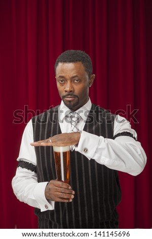 Well dressed African American male in retro suite holds hand over a glass of beer to say no drinking.