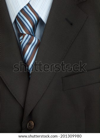 detail of mens pinstripe suit jacket lapel with  shirt and dark brown and blue colored striped tie