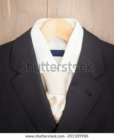 detail of mens suit jacket  shirt and tie on a hanger against wooden wardrobe background
