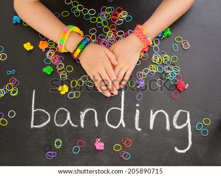 childs arm with loom band bracelets on a blackboard with the word banding and colorful elastic bands