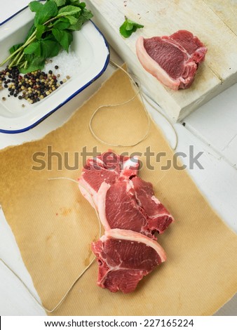 uncooked lamb chops  on brown paper with parcel string and herbs and spices and chopping board behind