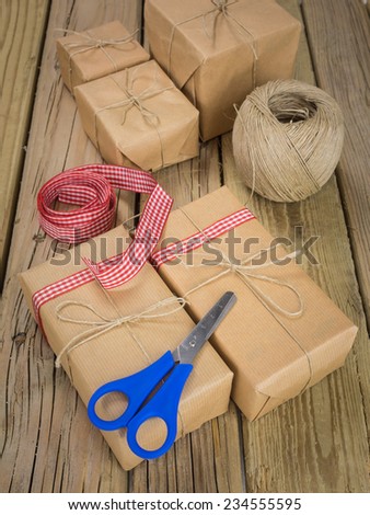 arrangement of  parcels wrapped with brown paper and string with ball of string red check ribbon and scissors against an aged wooden background