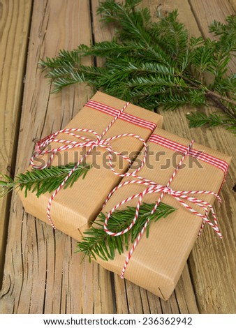 parcels wrapped in  brown paper with red and white string against an aged wooden background with conifer decoration and red and white checked ribbon