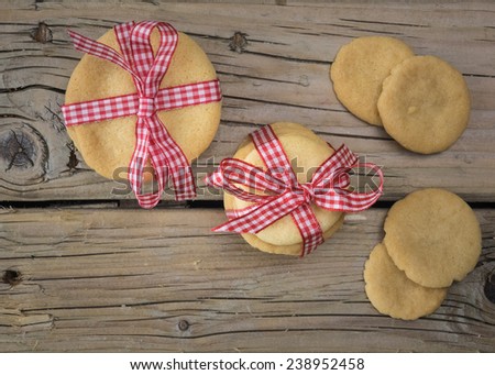 stacks of home baked cookies tied up with red and white check ribbon  with loose cookies against an aged wooden table top