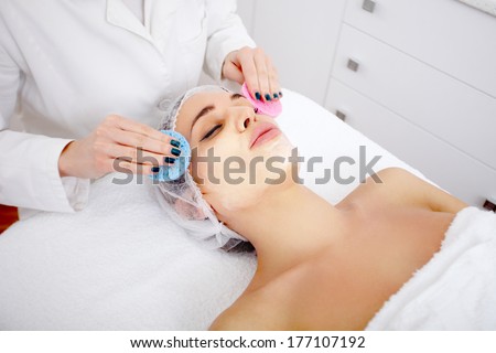 Young woman with fully applied organic facial mask receiving head massage at day spa salon