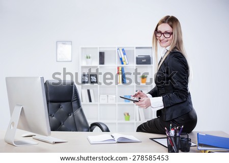 Business woman in her mid thirties sits on desk typing on tablet