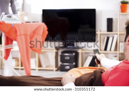 Man on the couch watching tv, changing channels,woman ironing in