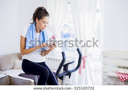 Sporty woman training on exercise bike using tablet in bright living room