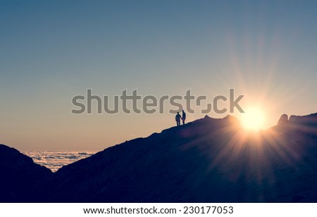 silhouette of a couple holding hands on a mountain ridge with sun rising
