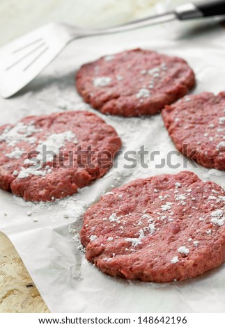 Four raw ground beef burgers on the wax paper
