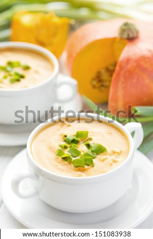 Creamy pumpkin bacon soup with green onion in two white bowls, autumn cuisine