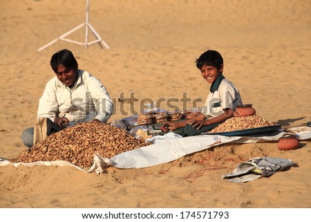 JAISALMER, INDIA - FEB 25: A street vendor with unidentified boy sells baked peanuts at the Sam Sand Dune on Feb 25, 2013 in Jaisalmer, India during the Desert Festival which is held in winter to attract tourists.